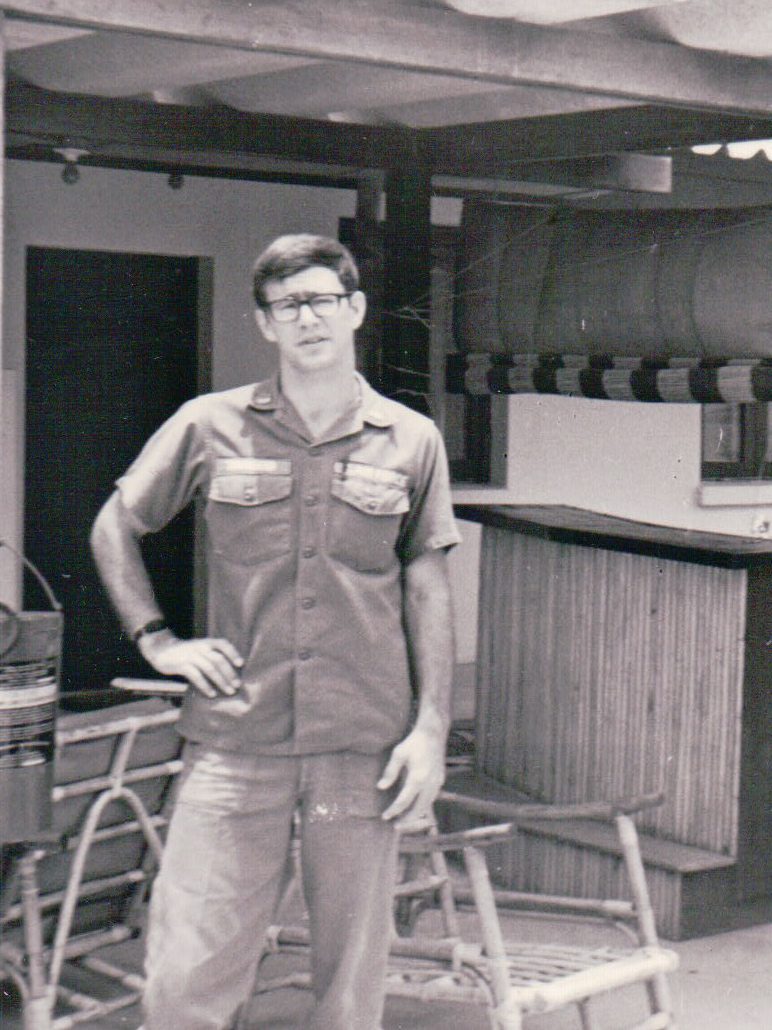 A young man in glasses and a uniform stands confidently indoors.
