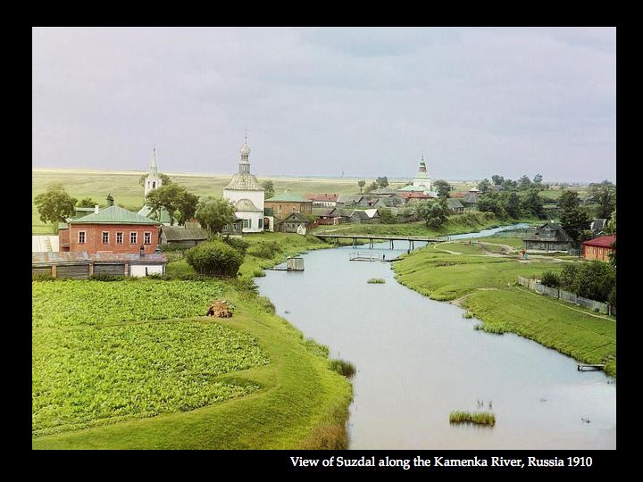 A serene river flowing through a green landscape with distant buildings.