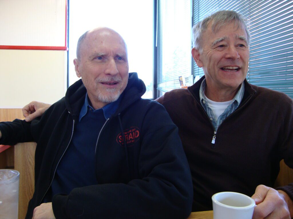 Two men sitting together, smiling warmly.