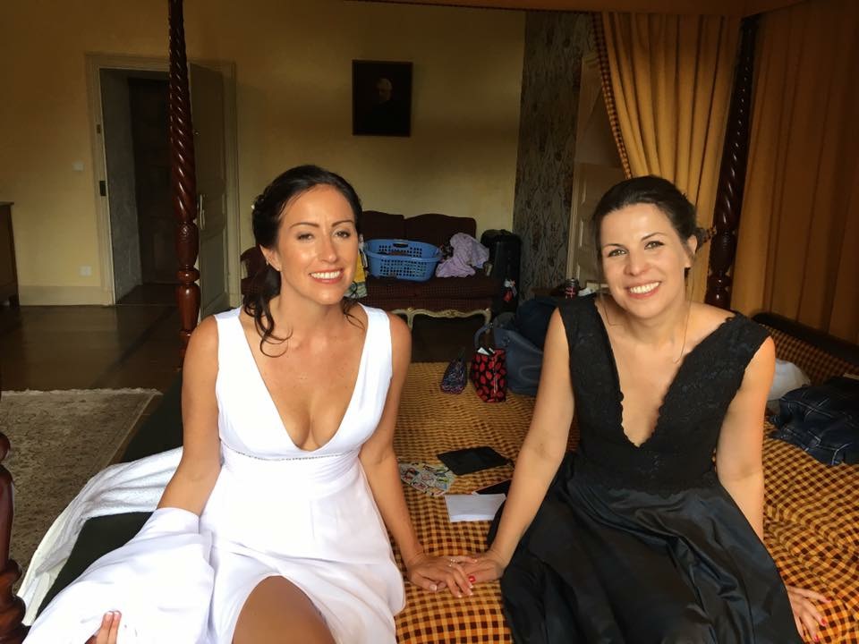 Two women in elegant dresses sitting indoors, smiling warmly.