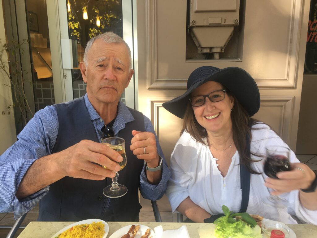 Two people enjoying drinks and a meal outdoors on a sunny day.