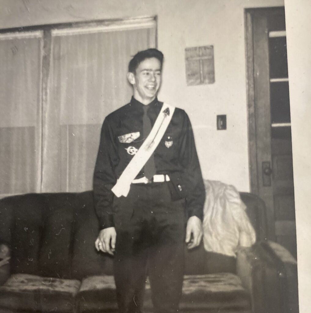 A man in formal military uniform posing indoors beside a couch.