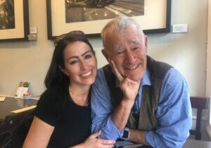 A young woman smiles warmly beside an elderly man in a cozy setting.