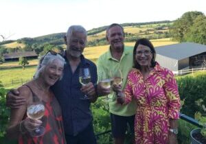 Four adults enjoying drinks outdoors with scenic countryside views.