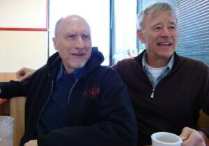 Two men sitting together, smiling warmly.