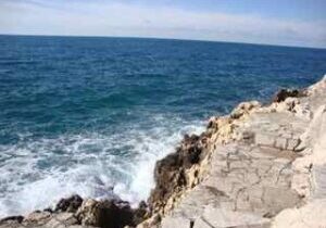 Waves crashing against rocky coastline under a clear sky.