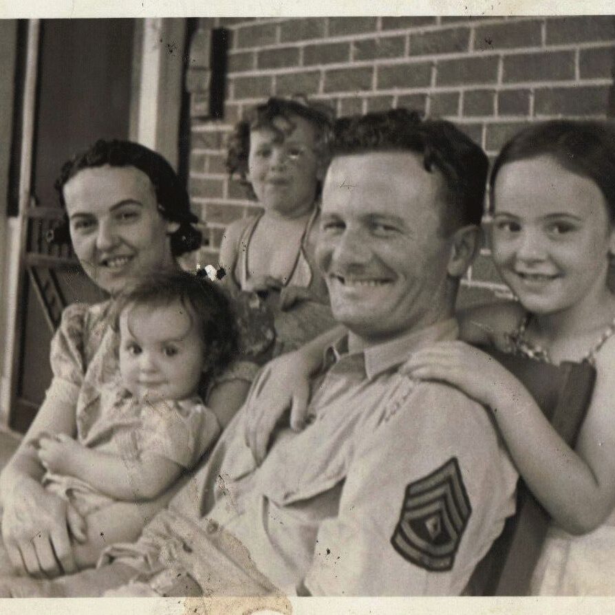 A joyful family portrait with parents and three children smiling together.