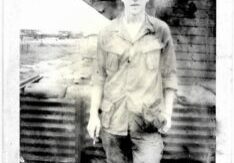 Black and white photo of a young man standing outdoors in casual clothes.