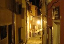 Narrow cobblestone street illuminated by warm streetlights at night.