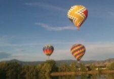 Three colorful hot air balloons float over a calm lake at sunset.