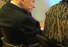 Elderly man in wheelchair talking to a woman in patterned clothing.