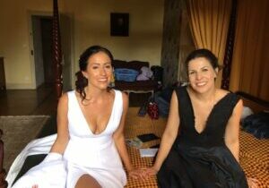 Two women in elegant dresses sitting indoors, smiling warmly.