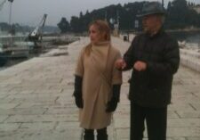 Two people walking arm in arm along a waterfront promenade.