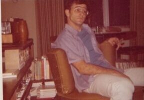 Robert is sitting on a brown chair in a cozy room.