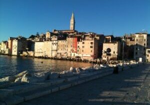 Coastal town with colorful buildings and a tall bell tower at sunset.