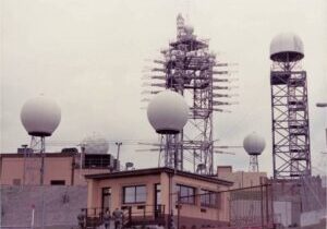 Radar station with large spherical antennas on rooftops and a central radar tower.