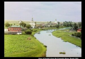 A serene river flowing through a green landscape with distant buildings.