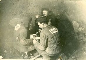 Soldiers inside a bunker during wartime, wearing numbered uniforms.
