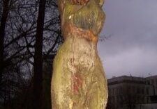 A weathered tree trunk carved into a humanoid figure outdoors.